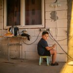 Ionuț se joacă la telefon pe prispa casei din Corcova, România, iulie 2017